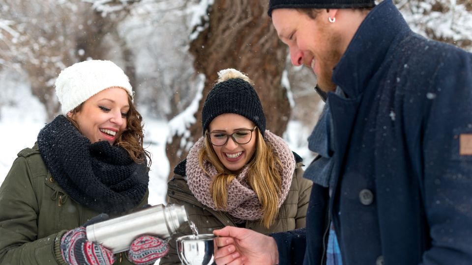 Three friends in winter clothing enjoy a hot drink together in a snowy outdoor setting