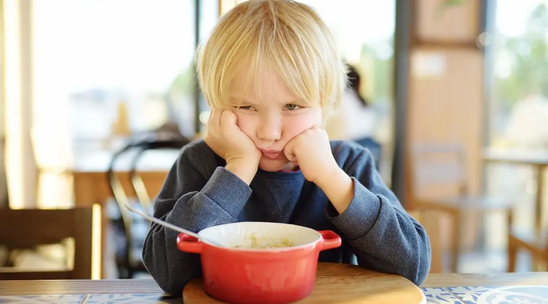 Enfant boudeur devant un bol de nourriture