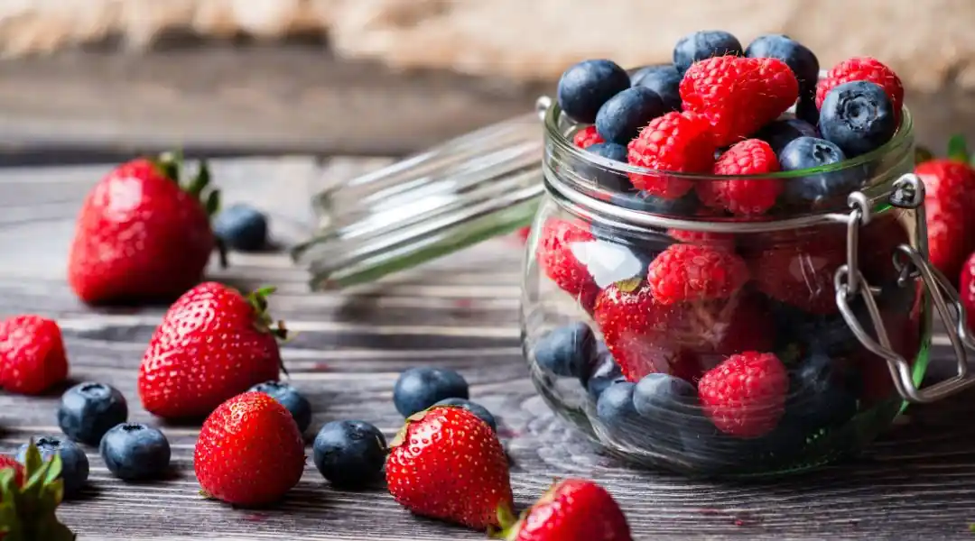 Bocal en verre rempli de fraises, myrtilles et framboises sur une surface en bois