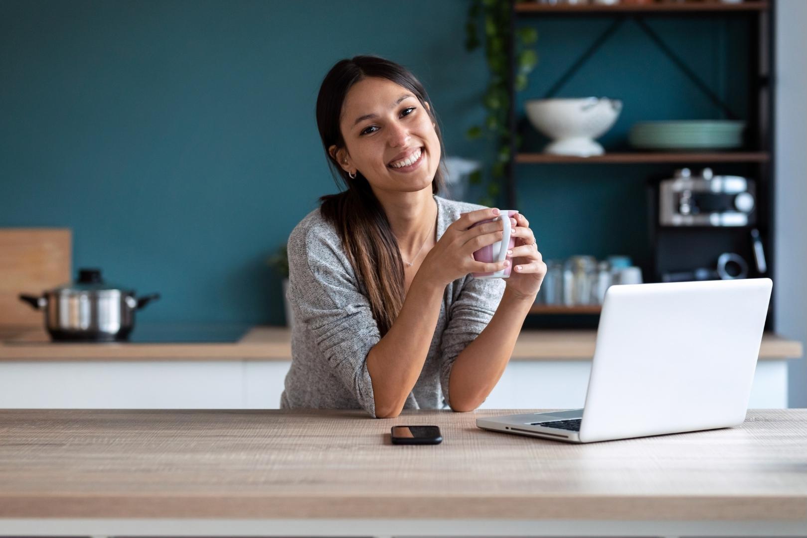 Nutritionniste souriante avec une tasse de café, assise devant un ordinateur | Smiling dietitian holding a coffee cup, sitting in front of a laptop