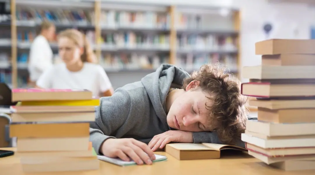 Adolescent endormi sur une pile de livres en bibliothèque