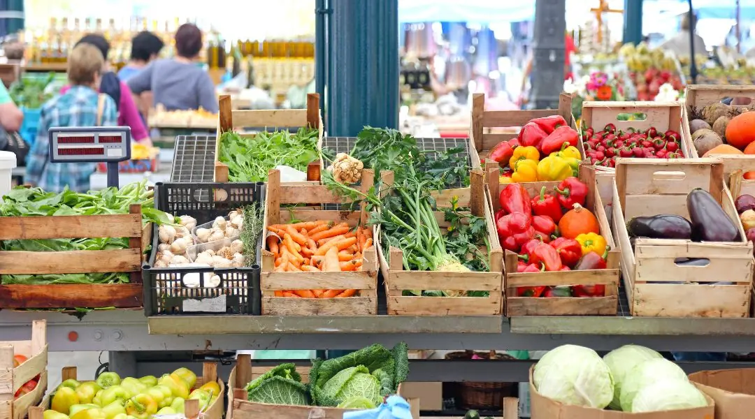 Étalage de marché avec des caisses en bois remplies de légumes frais comme des carottes, poivrons et choux