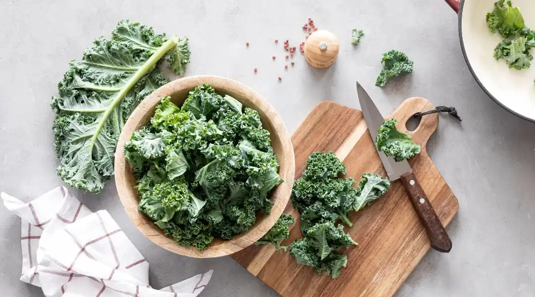 Feuilles de chou kale fraîches dans un bol en bois avec morceaux sur planche à découper