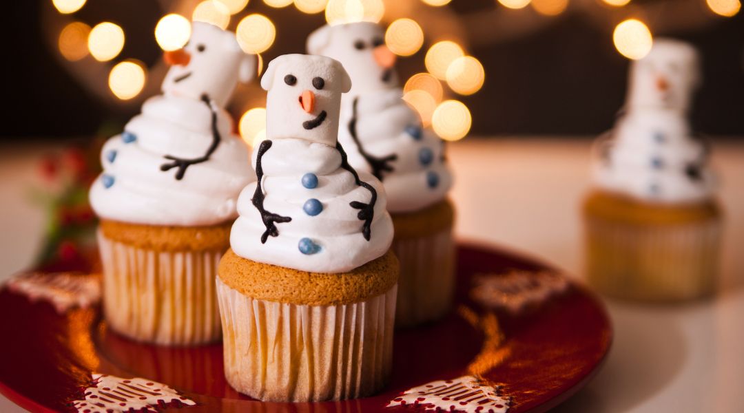 Des cupcakes festifs décorés avec des bonhommes de neige en guimauve, avec des visages souriants et des bras en forme de brindilles, sur une assiette rouge