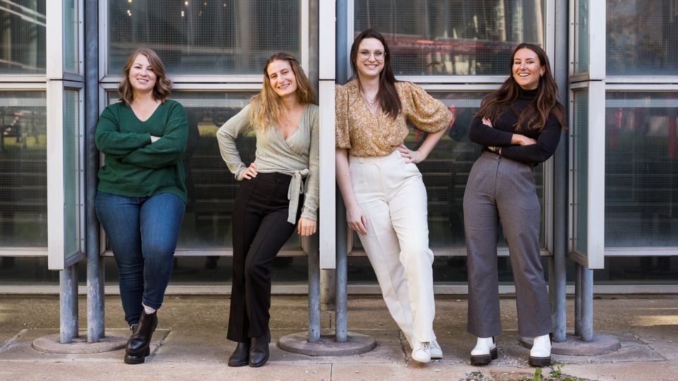 Four smiling TeamNutrition Dietitians Nutritionists pose confidently outside a modern glass building