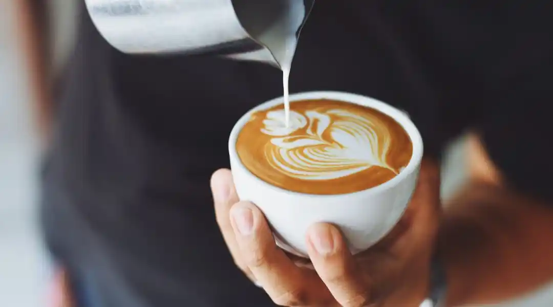 Barista versant du lait chaud dans un latte avec motif floral en mousse