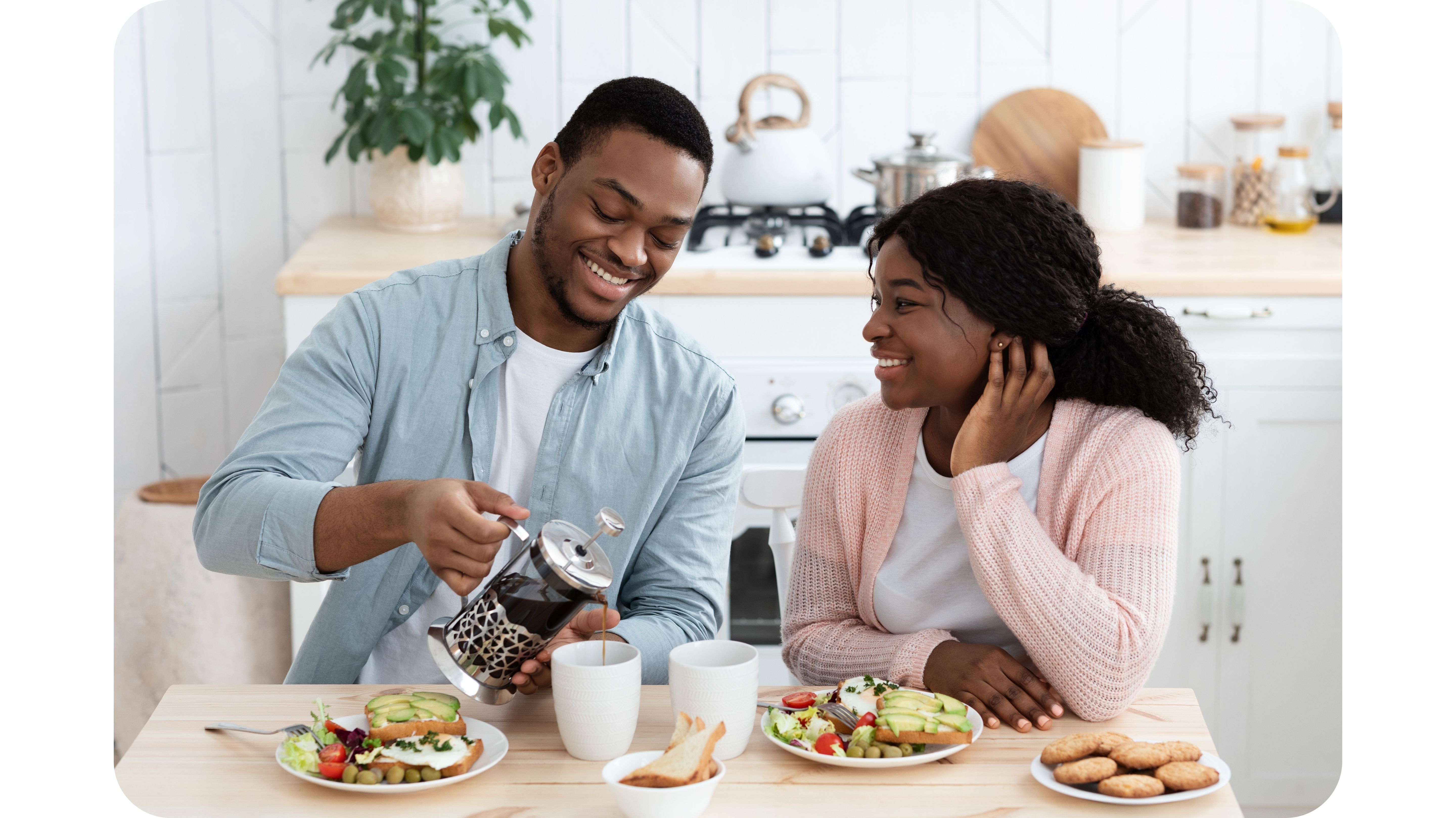 Couple souriant partageant un repas sain avec du café dans une cuisine lumineuse