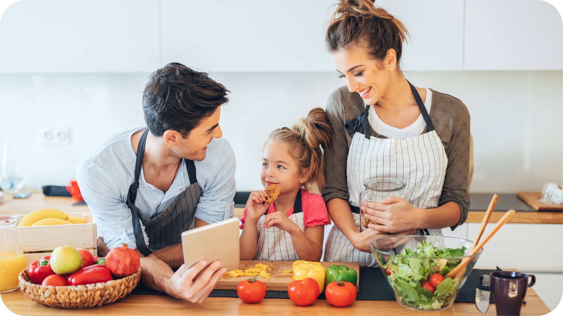 Famille préparant un repas sain ensemble dans la cuisine pendant que l'enfant mange un biscuit