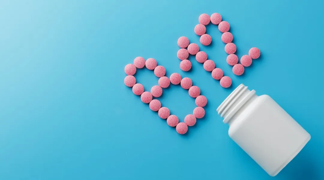 Comprimés roses de vitamine B12 formant un cœur et le mot “B12” à côté d’un flacon blanc
