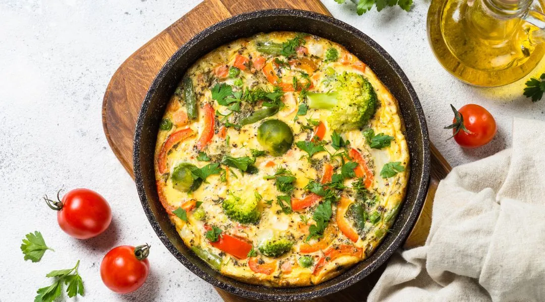 Frittata aux légumes avec brocoli, poivrons et herbes dans une poêle sur une planche en bois