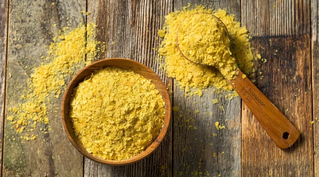 Bol et cuillère en bois remplis de flocons de levure nutritionnelle jaune sur table rustique
