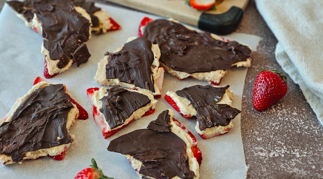 Strawberry hcocolate bark placed on parchment paper, with fresh strawberries nearby
