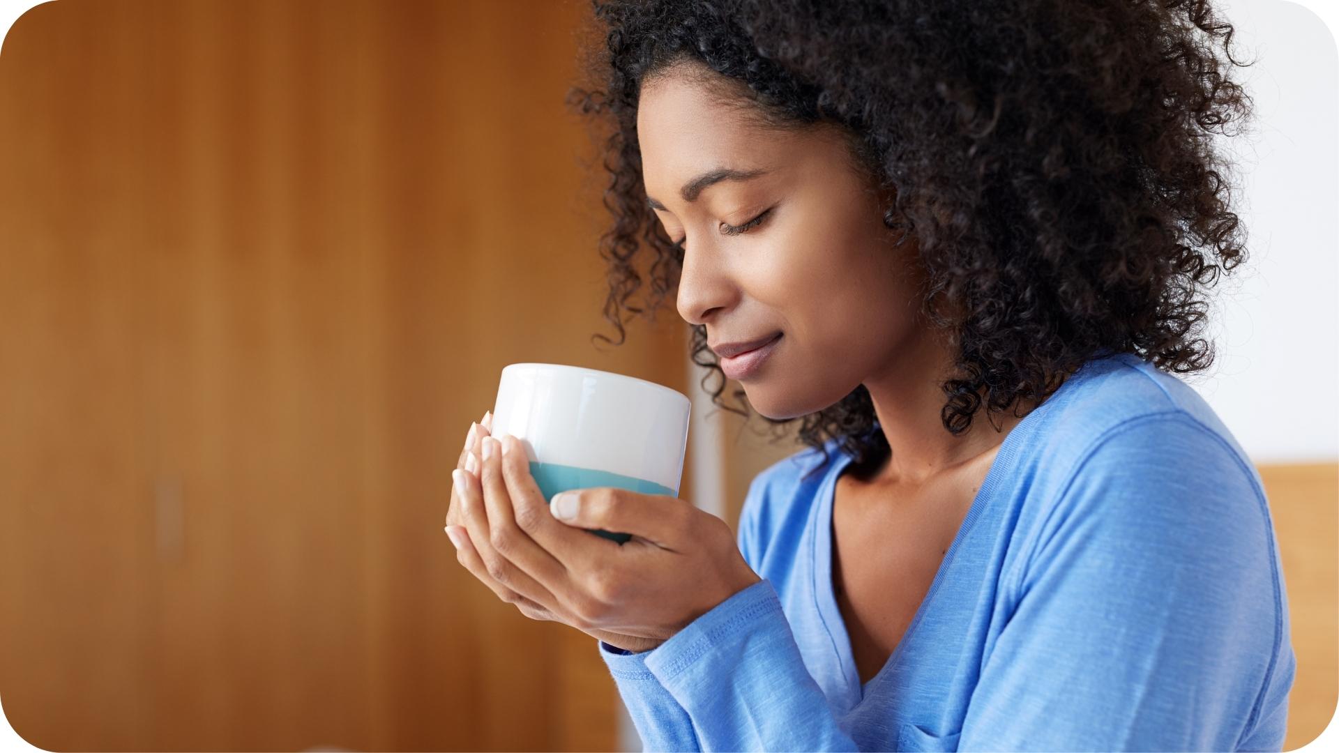 
Femme savourant une boisson chaude, les yeux fermés, tenant une tasse blanche