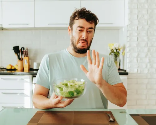 Homme faisant la grimace en tenant un bol de salade - Man grimacing while holding a bowl of salad